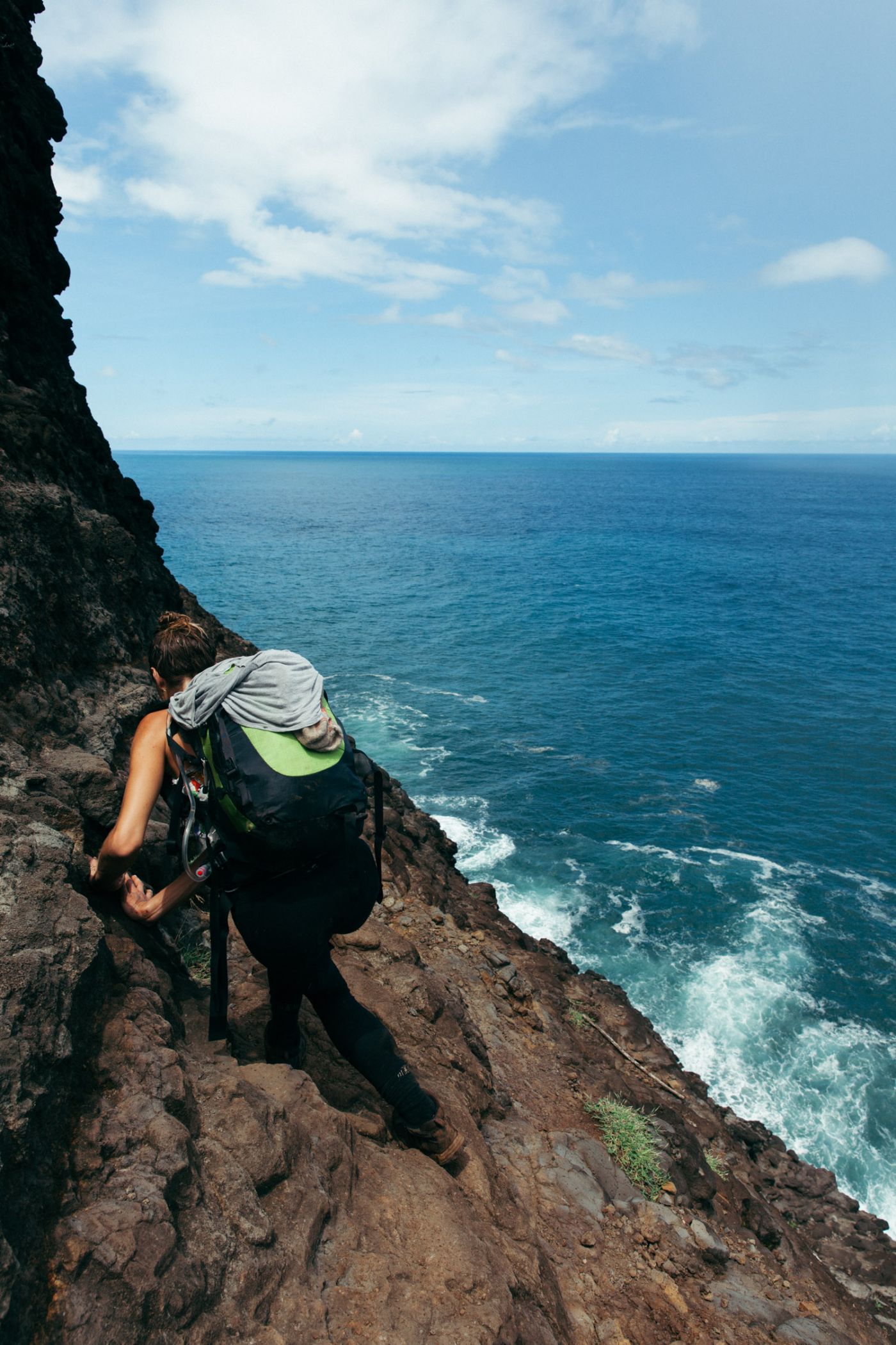 Woman hiking against a cliff over the water, Kalalau Trail, Kaua'i, Hawaii